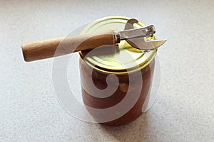 Glass jar with canned food and a can opener on the kitchen table, top view, space for text