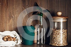 Glass jar with cereals, reusable shopping bag with nuts, reusable coffee cup and bamboo leaves on wooden shelf. Zero waste concept