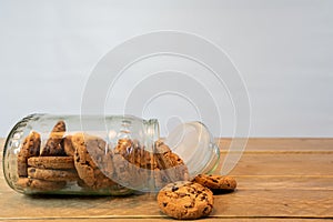 Glass jar with chocolate chip cookies on his side. Cookies out of the jar on the wooden table.