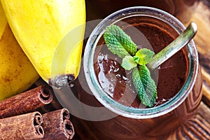 Glass jar with chocolate pudding or mousse with fresh banana, mint and cinnamon sticks over a wooden table. Sweet dessert