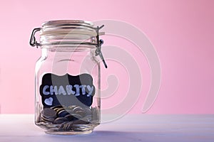 Glass jar with coins with chalk tag Charity on a pink background. Donation and charity concept. Copy space.