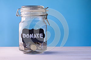 Glass jar with coins with chalk tag Donate on a blue background. Donation and charity concept. Copy space