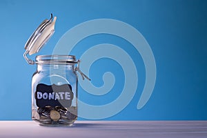 Glass jar with coins with chalk tag Donate on a blue background. Donation and charity concept. Copy space