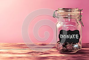 Glass jar with coins with chalk tag Donate on a pink background. Donation and charity concept. Copy space