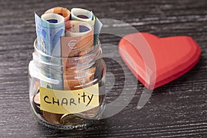 Glass jar with coins and euro notes with the inscription CHARITY. With a huge red heart