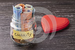 Glass jar with coins and euro notes with the inscription CHARITY. With a huge red heart