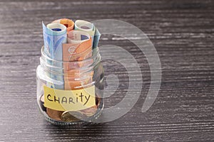 Glass jar with coins and euro notes with the inscription CHARITY. On the old black wooden table