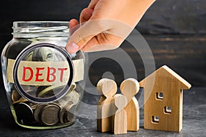 Glass jar with coins and the inscription ` Debt `, family and wooden house. Real estate, home savings, loans market concept. Payme