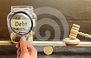 A glass jar with coins and the inscription `Debt` and the judge`s hammer are on the scales. Concept of financial crisis and probl