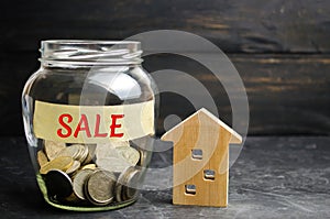 Glass jar with coins and the inscription `sale` and a small wooden house. real estate concept. sale of a home, apartment property
