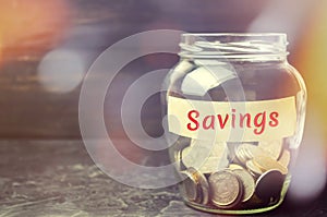 Glass jar with coins and the inscription `Savings`. The concept of accumulating money in the family budget. Family Insurance. Dist