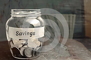 Glass jar with coins and the inscription `Savings`. The concept of accumulating money in the family budget. Family Insurance. Dist