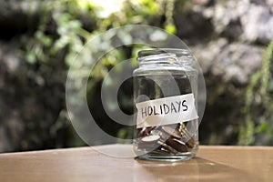 A glass jar with coins inside and a `vacaciones` tag on a wooden. Un bote de cristal con monedas dentro, tiene una etiqueta que po photo