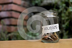 A glass jar with coins inside and a `vacaciones` tag on a wooden. Un bote de cristal con monedas dentro, tiene una etiqueta que po photo