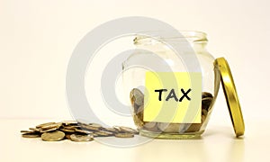 Glass jar with coins for savings. The inscription TAX on the note paper