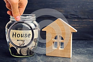 A glass jar with coins and a wooden house and the inscription `House`. The accumulation of money to buy a house. Rent an apartment photo