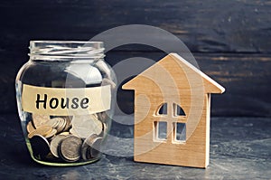 A glass jar with coins and a wooden house and the inscription `House`. The accumulation of money to buy a house. Rent an apartment