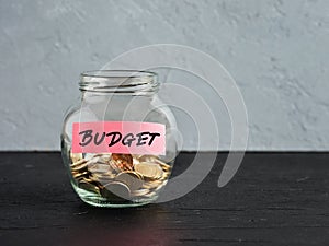 Glass jar with coins and the word budget on a label. Accumulating money for the family budget or education costs. Money saving and