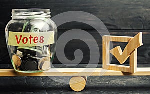 Glass jar with coins and the words `Votes` and a checkbox on the scales. Concept of voting for money. Bribing voters. Corruption i