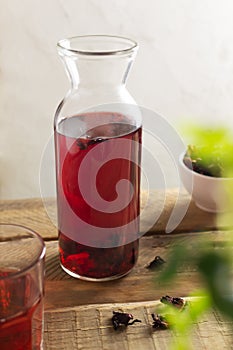 A glass jar with cold red hibiscus tea stands on a wooden table.