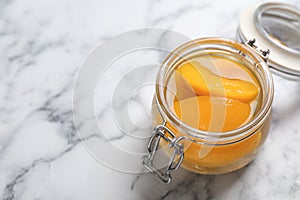 Glass jar with conserved peach halves on marble background