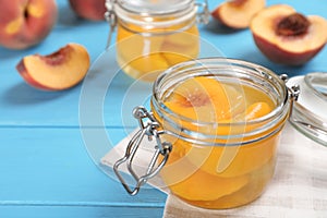 Glass jar with conserved peach halves on wooden table