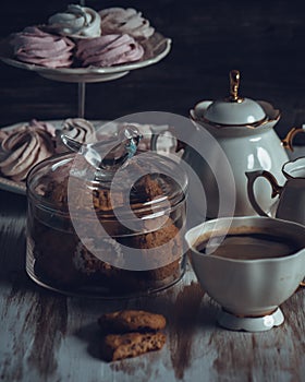 A Glass jar with cookies and a cup on a wooden table on dark background. Vintage Style