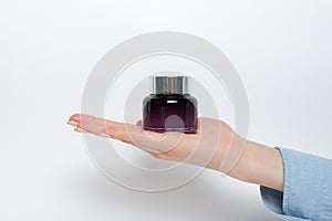 Glass jar for cosmetics in a female hand. White background