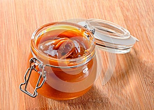 Glass jar  with cream  caramel sauce close-up on wooden background