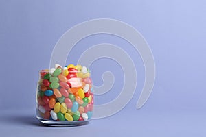 Glass jar with delicious bright jelly beans on color background