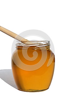 Glass jar with delicious fresh honey. There is a wooden ladle nearby. White isolated background.