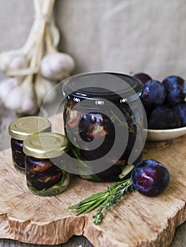 Glass jar with dried plums and fresh rosemary on wooden serving board, selective focus.