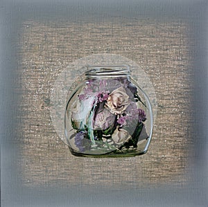 Glass jar with dry roses in front of canvas