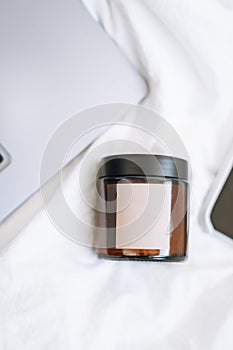 Glass jar with empty label on white sheets, bed linen background, mockup