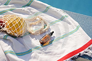 Glass jar of facial serum and bag of fruit on beach towel near blue swimming pool. The concept of skin care, beauty, aesthetic