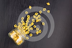 Glass jar filled with dry farfalle pasta and scattered around on black background