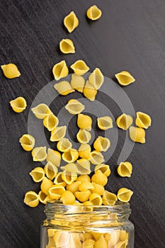 Glass jar filled with dry farfalle pasta and scattered around on black background