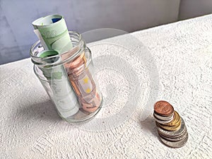 Glass Jar Filled With Euro Banknotes and Coins on Table. Concept of savings ranging from small money to large