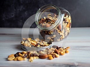 Glass jar filled with healthy nuts, seeds and raisins spilling out, the perfect health fat and good carbohydrate to provide