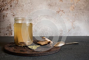 A glass jar of fresh beef bone broth with spices on an aged round stand and a vintage spoon on the side.