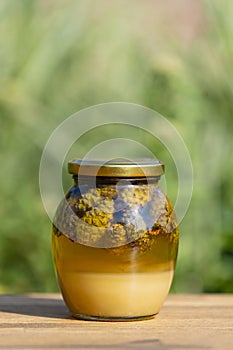 Glass jar of fresh honey with pine cones on a wooden table, closeup