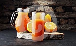 Glass jar of fresh orange juice with fresh fruits on dark table.