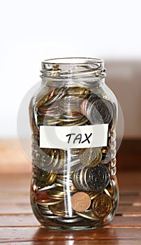A glass jar full of coins with tax written on a masking tape