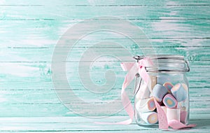 Glass jar full of colorful sweet marshmallows on turquoise wooden background.