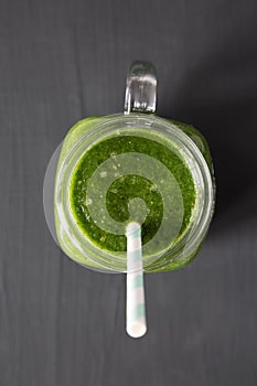 Glass jar full of green smoothie with spinach, avocado and banana over black background, top view. Flat lay, overhead, from above