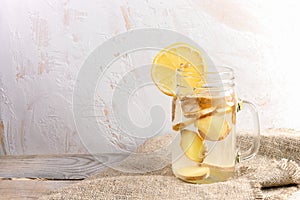 Glass jar with ginger water on burlap on wooden table on light background.