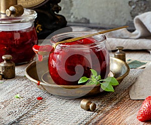 Glass jar with homemade canned strawberry jam, marmalade, jelly on rustic wooden grey table with basil