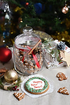 A glass jar of homemade gingerbread cookies, cinnamon sticks and other decoration elements against a backgrou