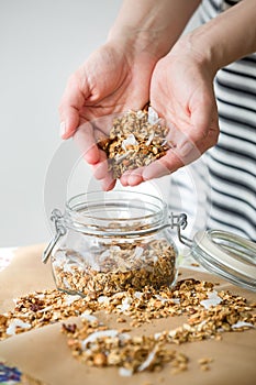 Glass jar of homemade organic granola with coconut and pecans on the baking paper background. Delicious breakfast cereal