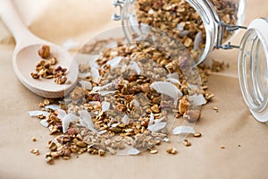 Glass jar of homemade organic granola with coconut and pecans on the baking paper background. Delicious breakfast cereal